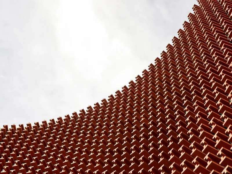 Upward view of terracotta brick lattice pattern forming a diagonal facade under overcast sky