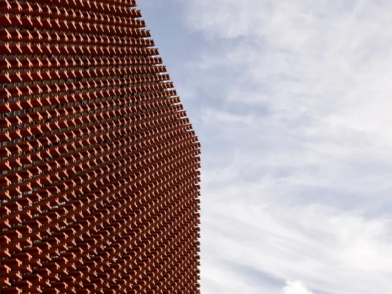 Angled surface of textured brick screen with protruding elements creating depth under cloudy skies
