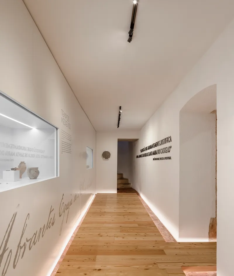 Gallery corridor with timber flooring, white walls, linear floor lighting, and display niches containing artifacts
