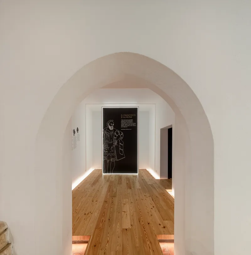 View through whitewashed stone arch toward gallery space with backlit graphic panel on far wall