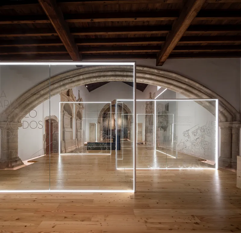 Illuminated glass panel installation beneath exposed timber beams in a vaulted gallery with stone arches
