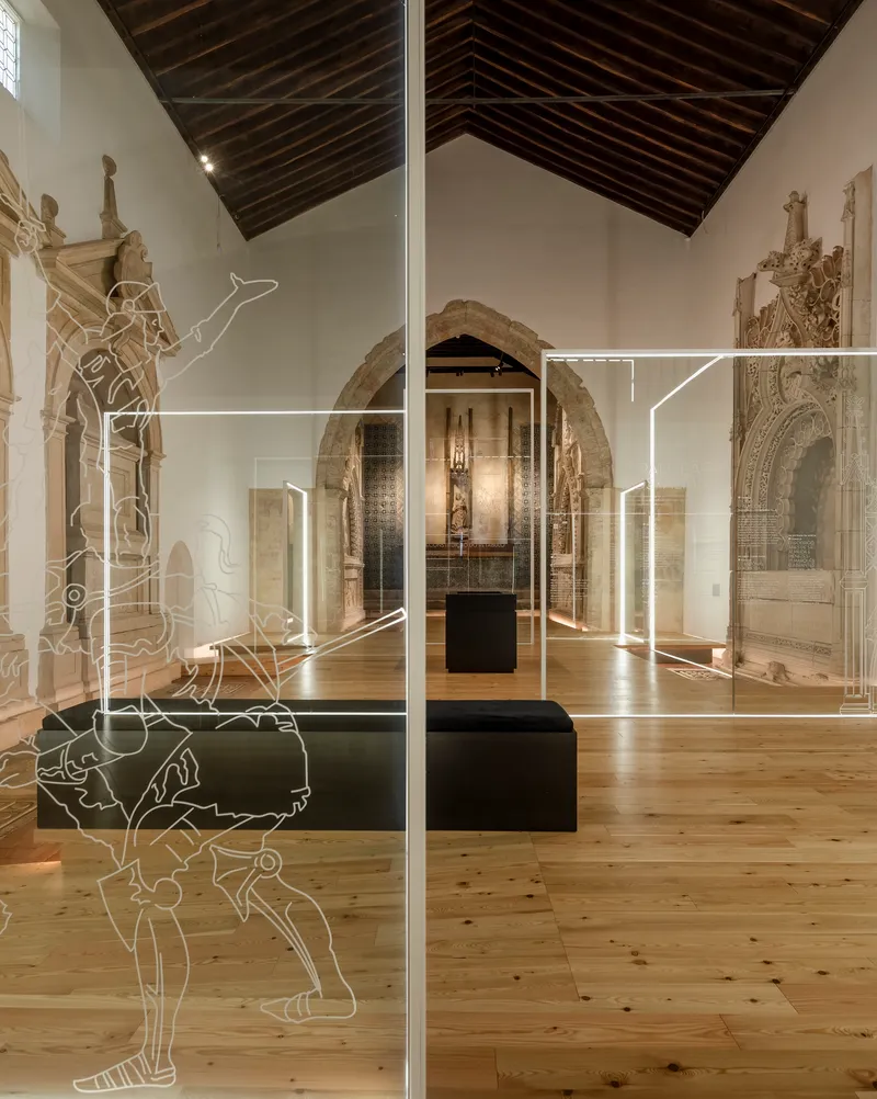 Glass partition with etched line drawings dividing a timber-floored nave with stone portals and rafters