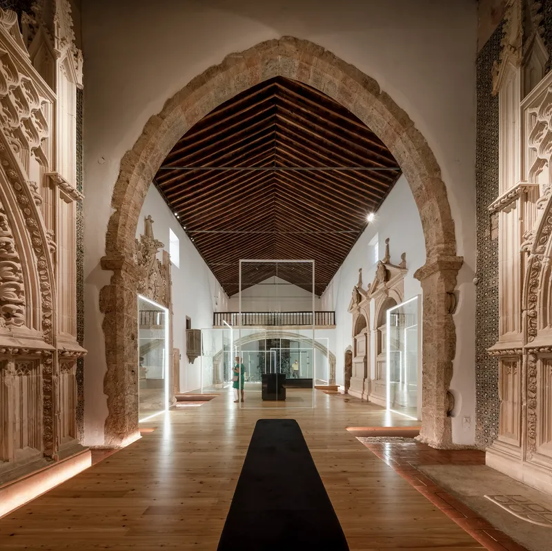 Long view through carved stone archway toward mezzanine beneath exposed timber vault and dark ceiling boards