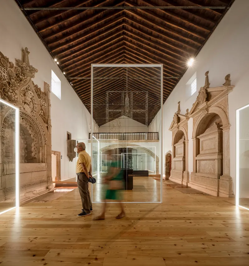 Visitors standing near glass display box in a gallery with carved stone tombs and timber roof