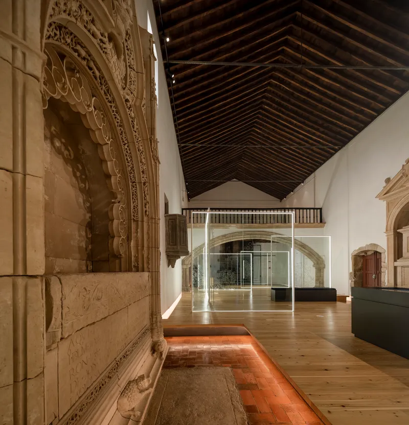 Gallery interior with carved stone portal, exposed timber ceiling and illuminated glass partitions on timber floor