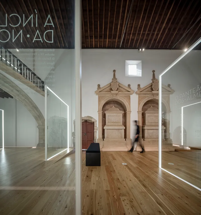 Stone tomb monuments framed by glass panels with LED edges and a visitor passing through