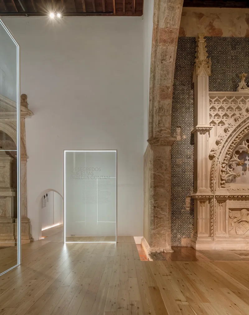 Backlit glass partition with etched inscription standing beside a weathered stone column and tiled wall