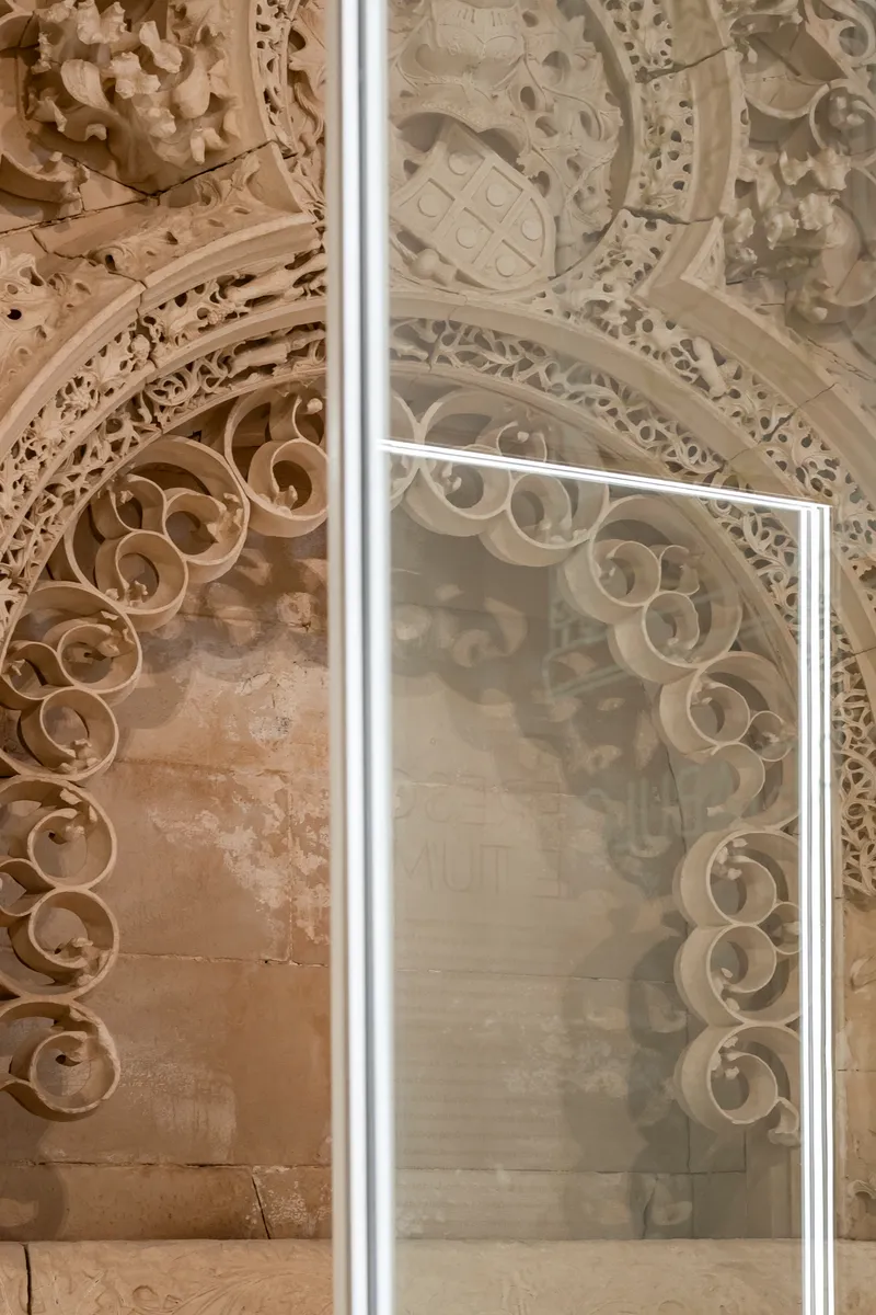 Detail of glass panel edge bisecting ornate carved stonework with decorative scrolls and heraldic symbols