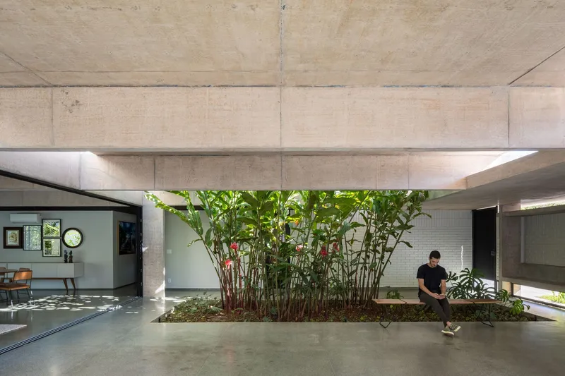 Interior courtyard planted bed with tropical foliage beneath board-formed concrete beams and a person seated