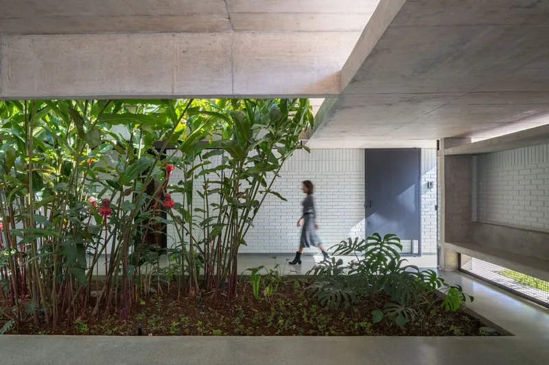 Interior garden bed with traveler's palms beneath concrete beams while a figure walks along white tiled corridor
