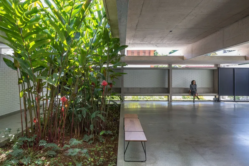 Covered passage with planted bed of palms beside polished concrete floor and a person standing near screened openings