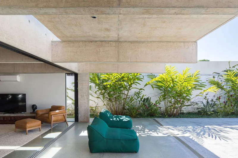 Poolside terrace with teal lounge chair casting shadows beneath concrete beam and planted garden wall