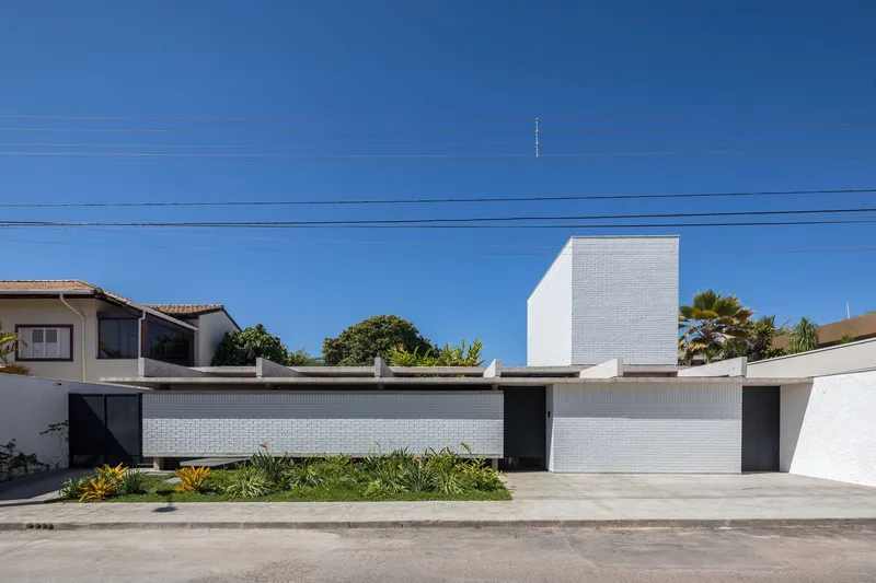 Street view of the white brick facade with planted bed and palm trees under clear blue sky
