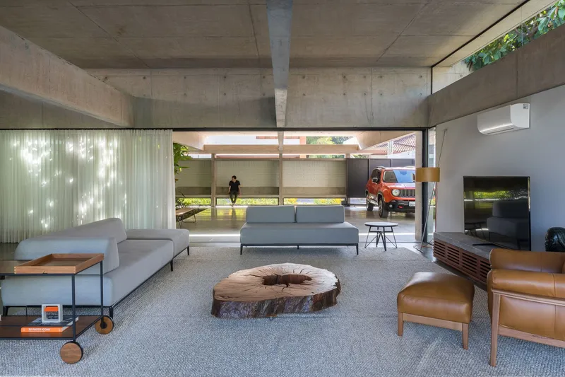 Living area with exposed concrete ceiling beams and clerestory windows filtering dappled sunlight onto the floor
