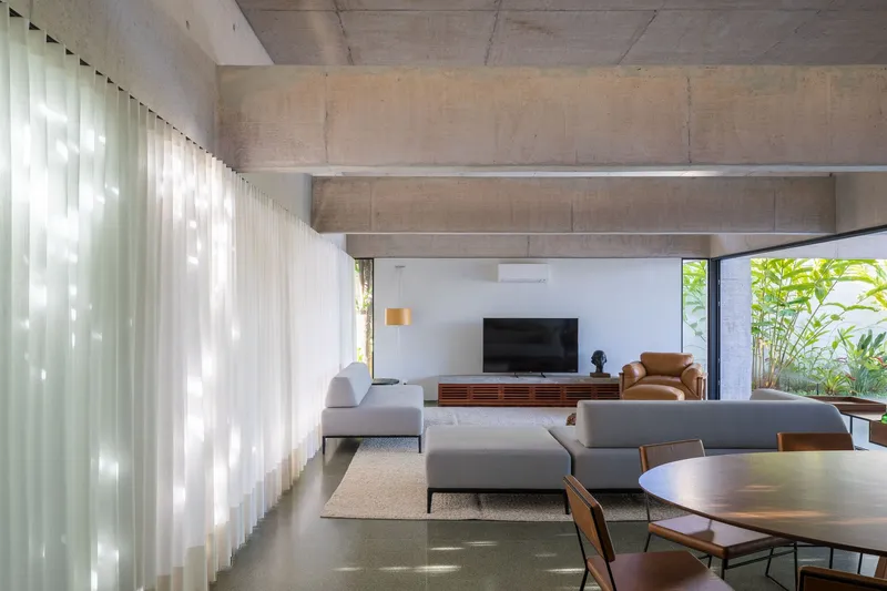 Living room corner with sheer curtains catching afternoon light beside a planted courtyard opening