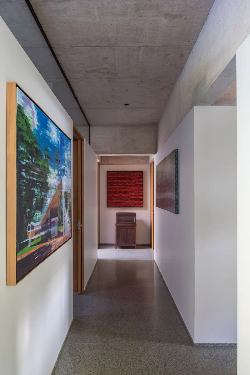 Hallway with board-formed concrete ceiling, white walls displaying artwork, and terrazzo flooring