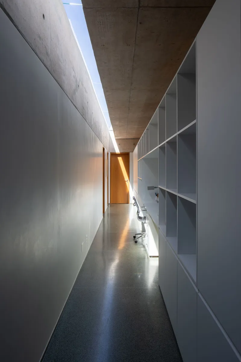 Corridor with clerestory skylight above, built-in shelving on one side and polished concrete floor