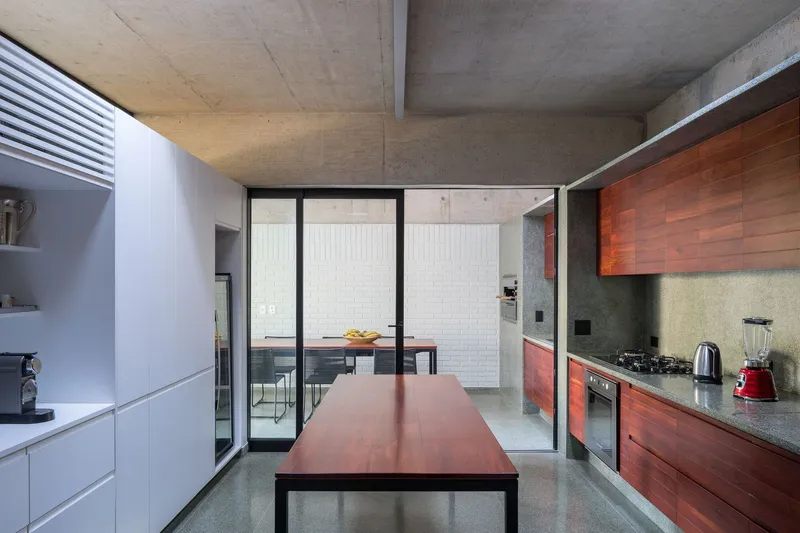 Kitchen with exposed concrete ceiling, timber cabinetry, and glazed doors opening to an exterior courtyard