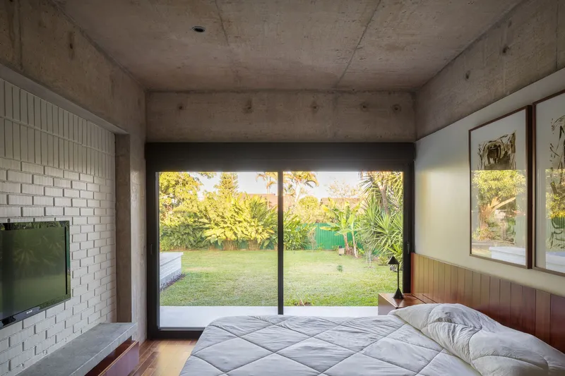 Bedroom with white brick accent wall and sliding glass doors overlooking a backyard lawn at sunset
