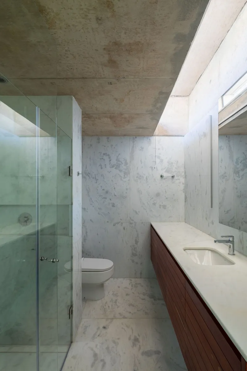 Bathroom with exposed concrete ceiling, walls and floor, glass shower enclosure and walnut vanity cabinet