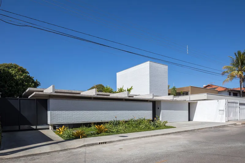 Street view showing white tile facade, horizontal metal fence and planted bed with palm trees