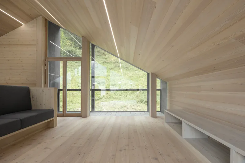 Light wood interior with sloped ceiling, linear lighting and full-height glazing overlooking hillside