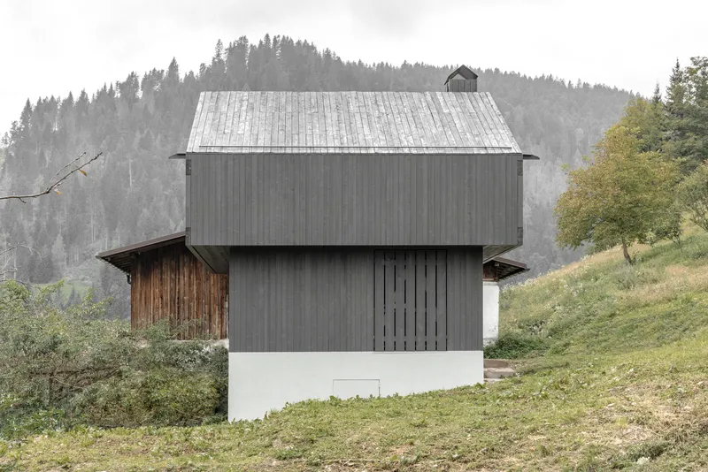 Two-story timber clad volume on a grassy slope with misty forested mountains in the background