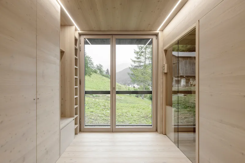 Timber-lined entrance hall with glazed door opening to a green meadow and distant mountains