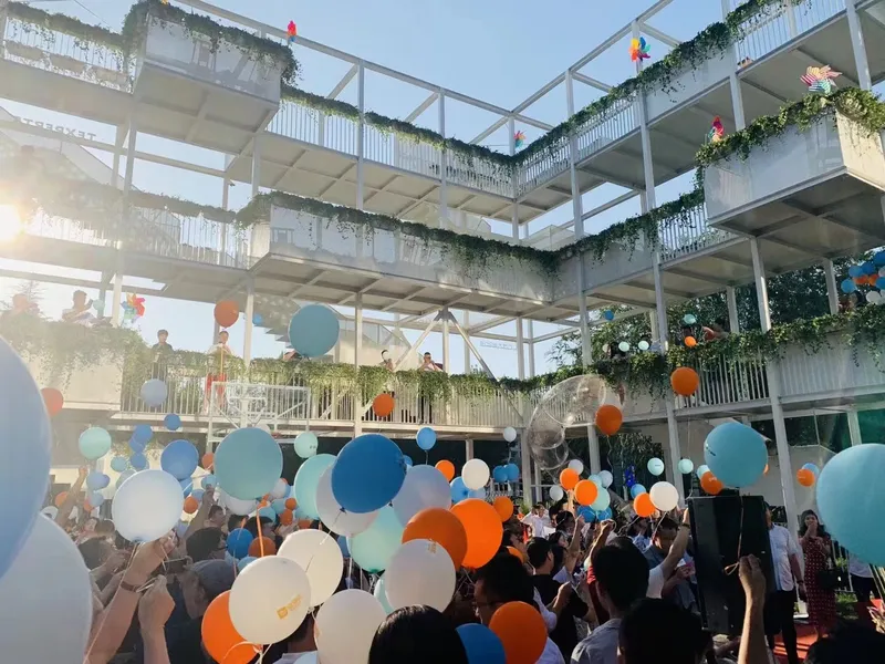 Upward view through released balloons toward planted balconies with white railings in afternoon sunlight