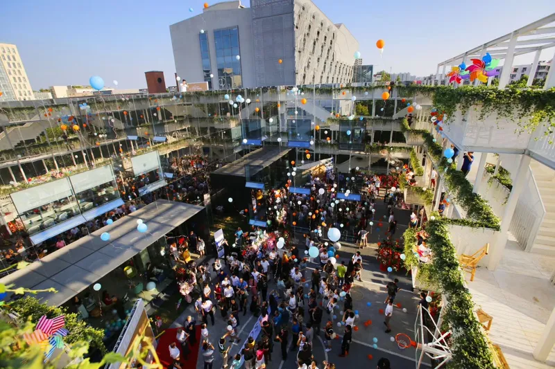 Aerial view of courtyard celebration with balloons rising past terraced units and planted green edges