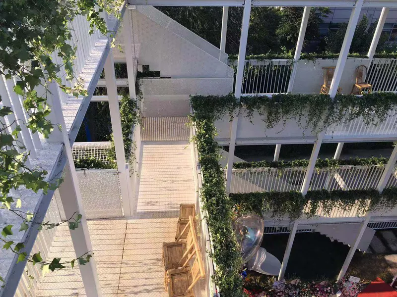 Elevated timber walkway threading through white structural frame with planted balconies and suspended slide