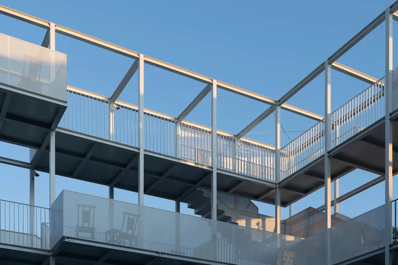 Stacked terrace levels with white steel frame and corrugated metal railings under clear sky