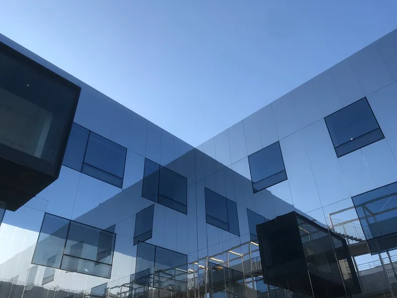 Courtyard view showing white and grey panels with irregularly placed protruding windows at dusk
