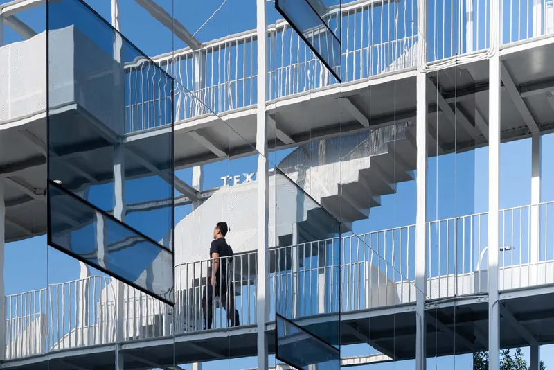 Close-up of external staircases with white railings and a figure walking across a bridge