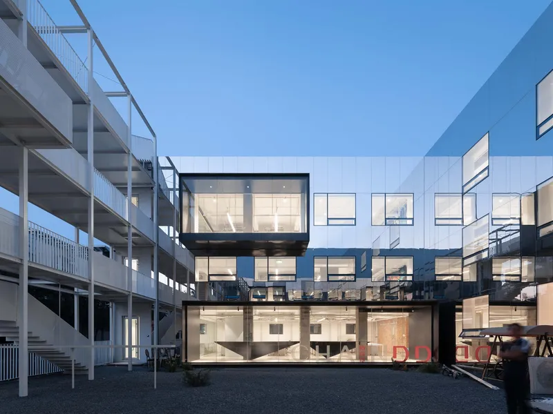 Illuminated glass facade showing interior office spaces at dusk in the courtyard