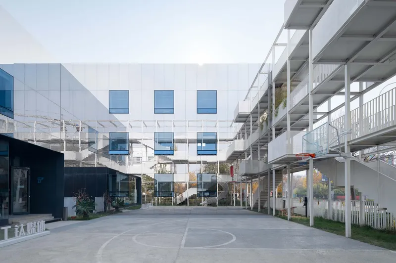White panel facade with recessed blue windows flanked by open structural frame and planted courtyard below