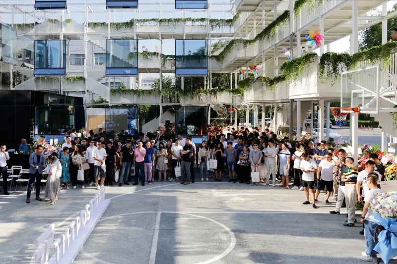 Courtyard gathering with residents assembled below planted terraces and cascading greenery on balcony edges