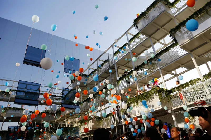 Rising balloons in courtyard framed by planted concrete terraces and white structural columns overhead