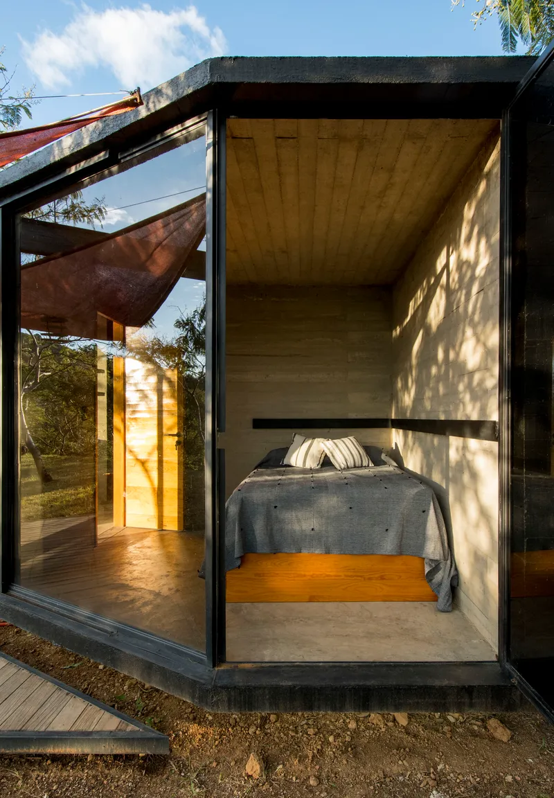 Sleeping alcove with glass sliding doors and dappled tree shadows on concrete walls