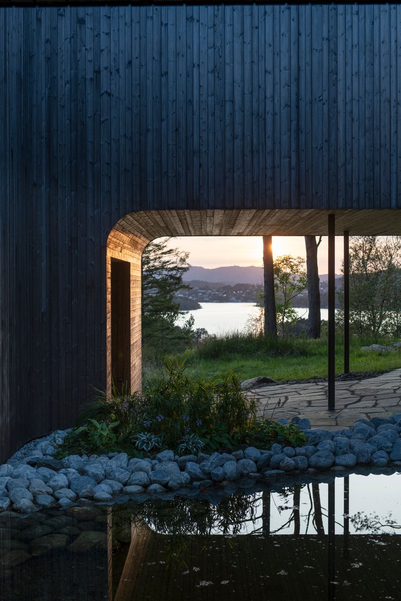 Covered passage with timber-lined soffit framing a view across the water at sunset