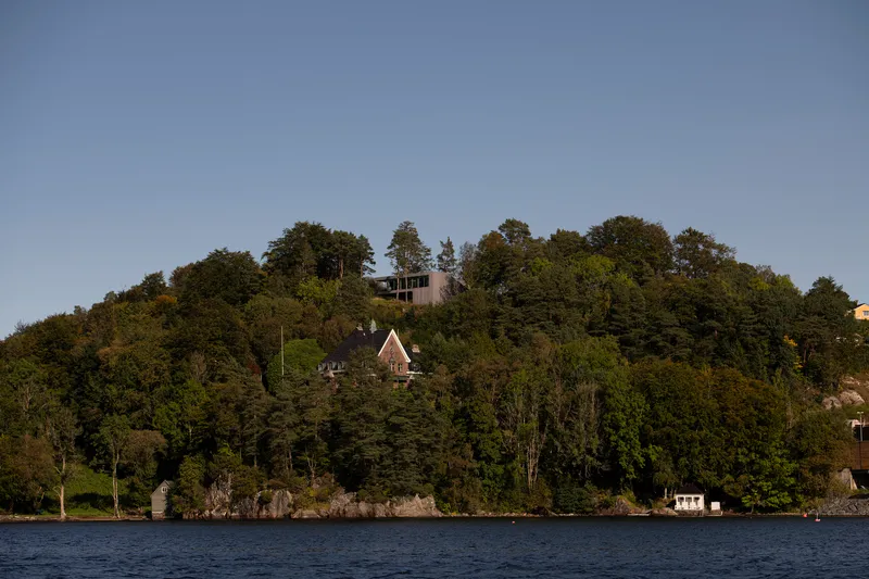 View from the water of forested hillside with residence visible at the crest