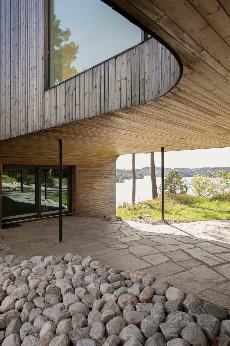 Covered terrace with flagstone paving and river cobbles beneath cantilevered timber and weathered wood volumes
