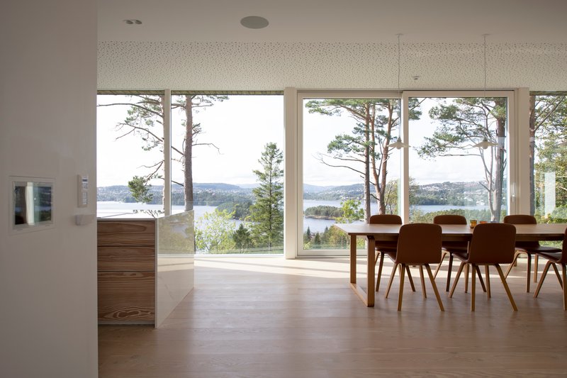 Dining area with floor-to-ceiling windows framing views of water and pines beyond