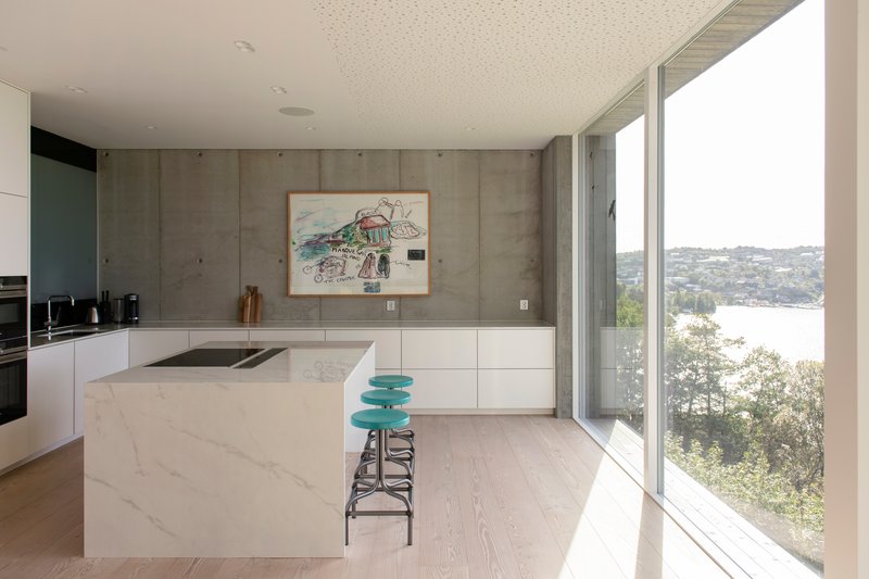 Kitchen with white island and concrete wall opening to water view through glazing