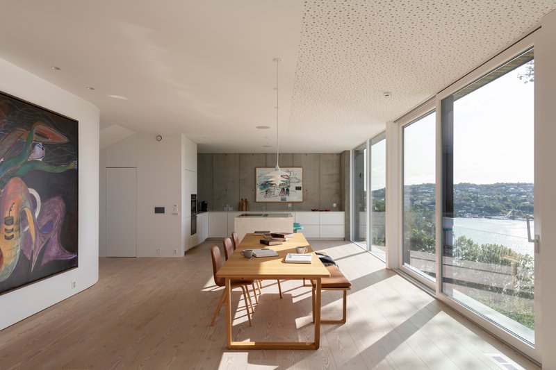 Open dining and kitchen space with timber table and floor-to-ceiling windows overlooking the bay