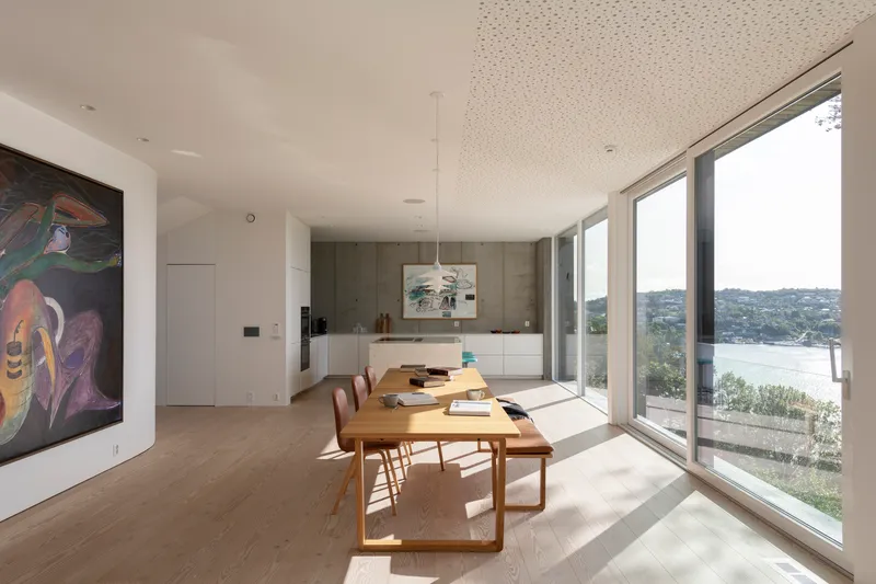 Open dining and kitchen space with timber table and floor-to-ceiling windows overlooking the bay