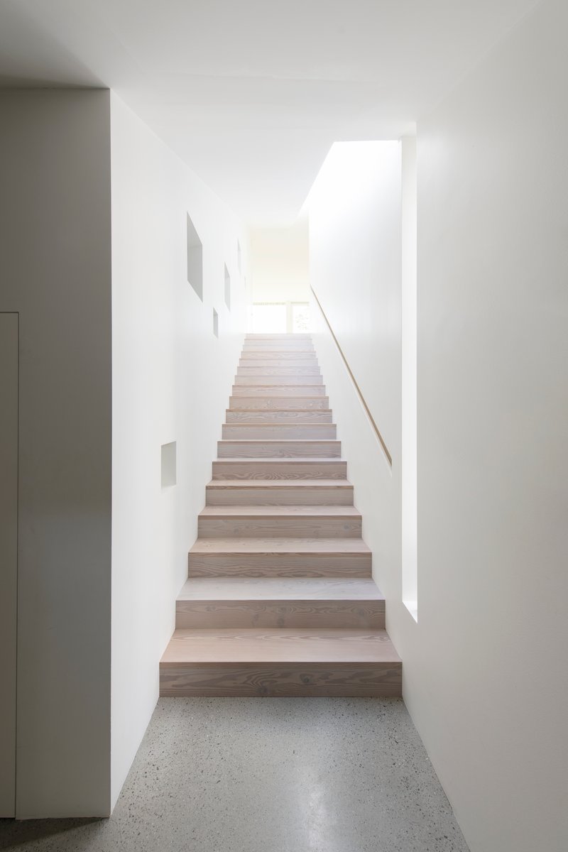 Timber staircase ascending through white walls with skylight above