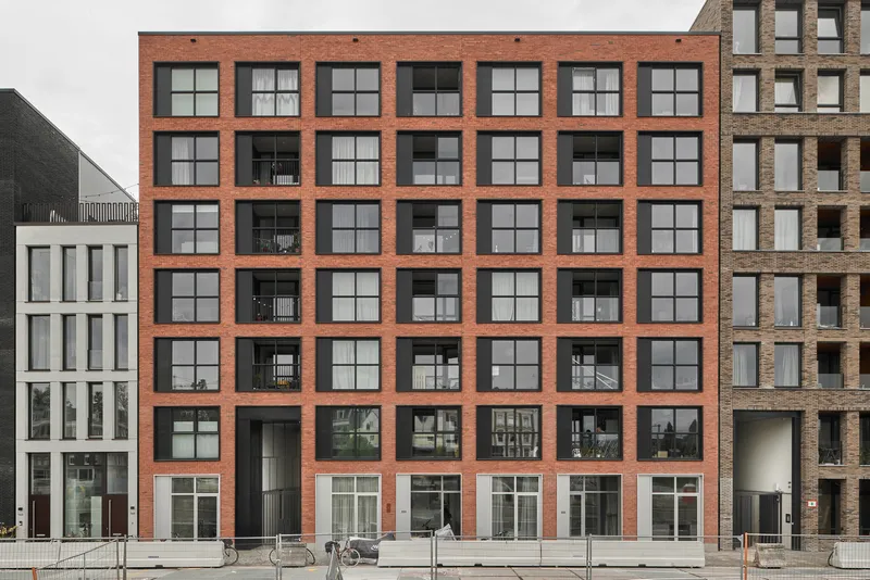 Facade with orange brick grid framing black recessed balconies and gridded windows at ground level