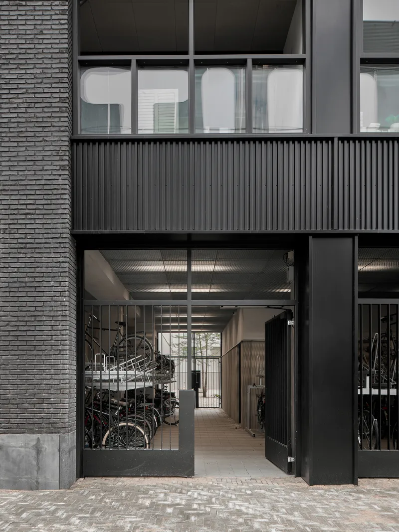 Ground-floor entrance with glazed doors opening to bicycle storage beneath corrugated metal ceiling