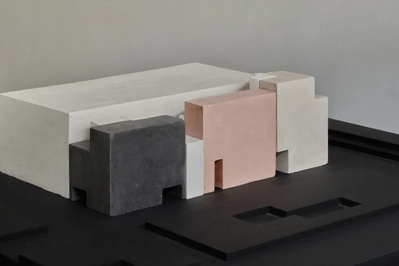 Physical massing model with white, pink, and grey volumes arranged on a black base